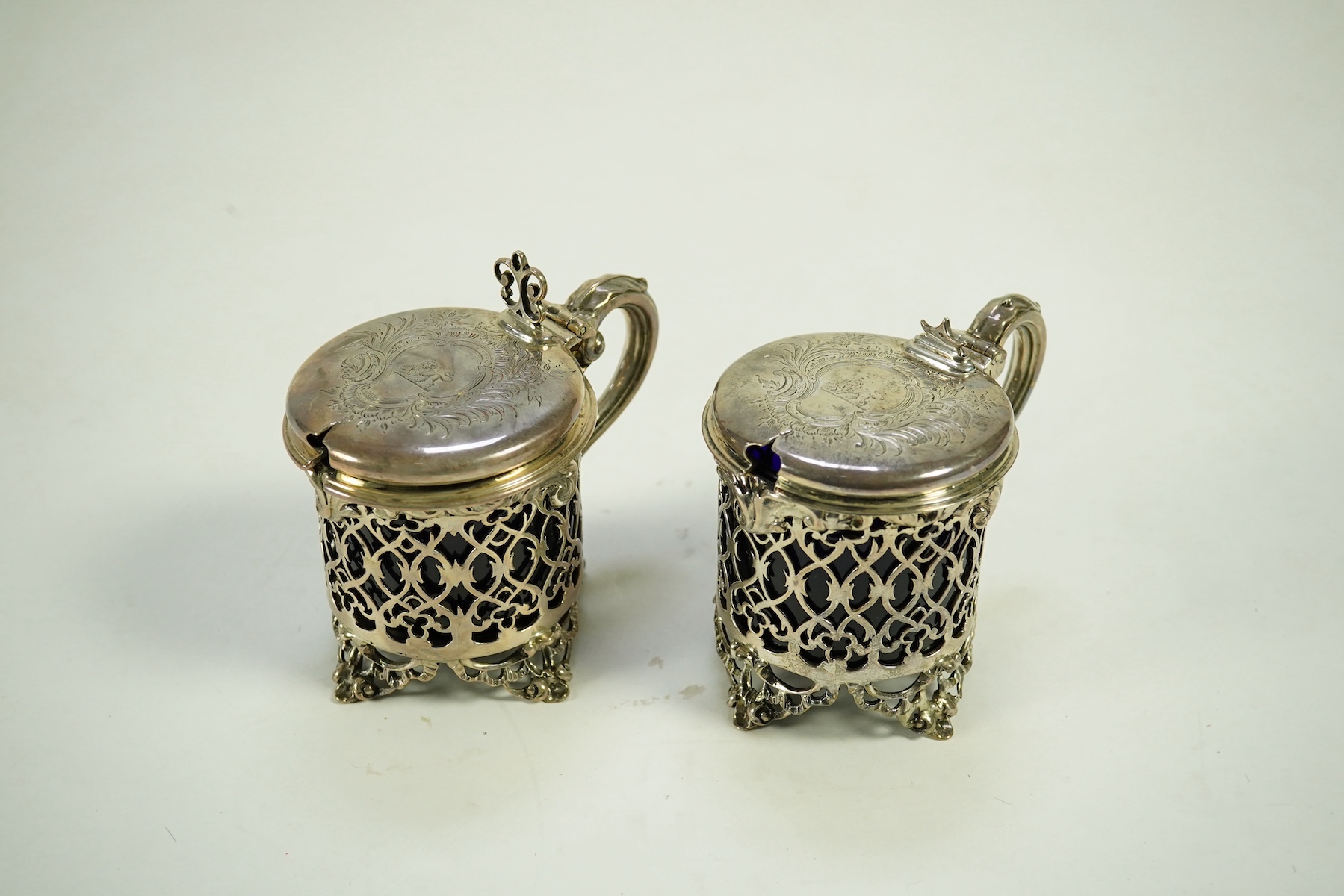 A near pair of ornate Victorian pierced silver drum shaped mustard pots and covers, one by Charles Thomas Fox & George Fox, the other by George Fox